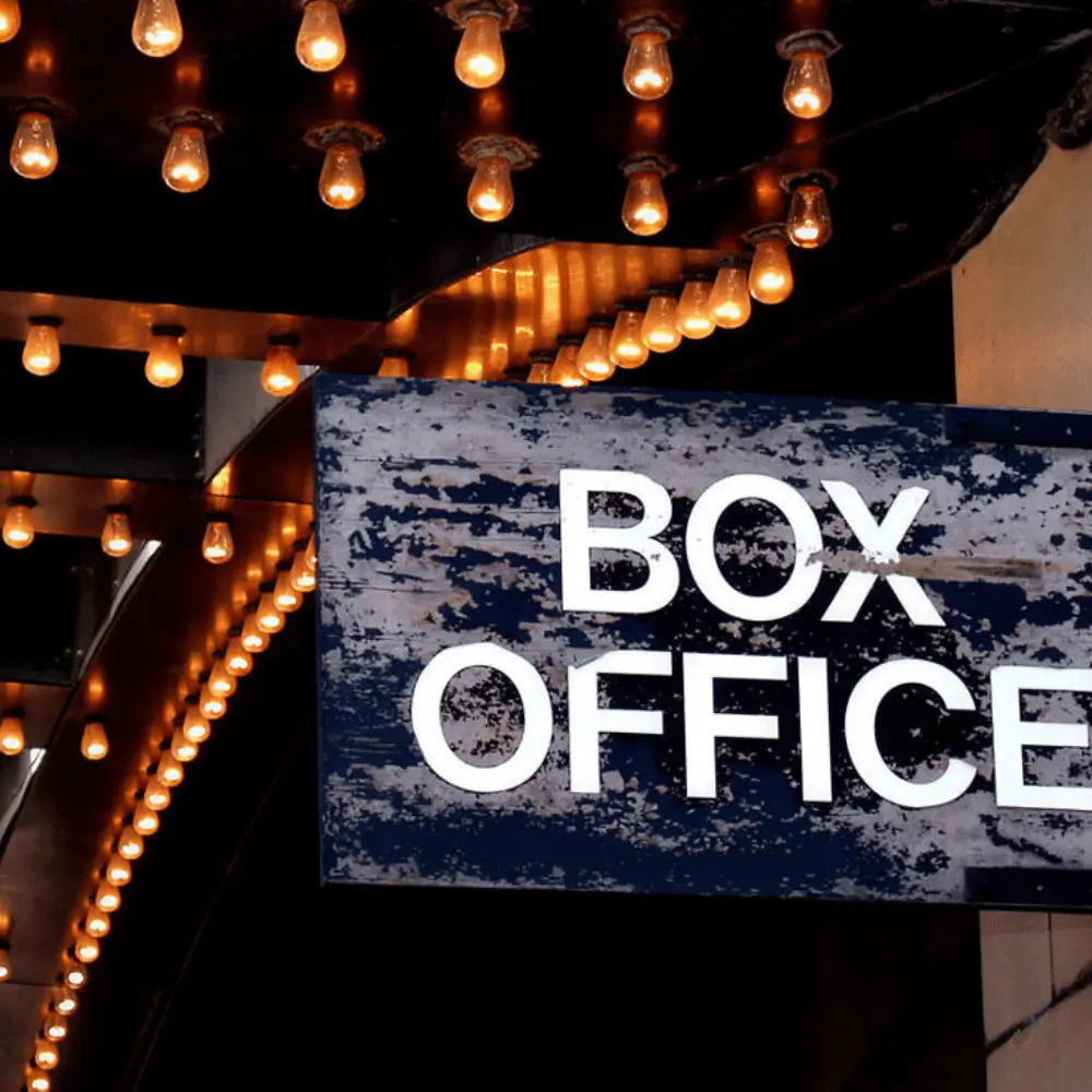 A weathered box office sign hanging beneath rows of glowing marquee light bulbs