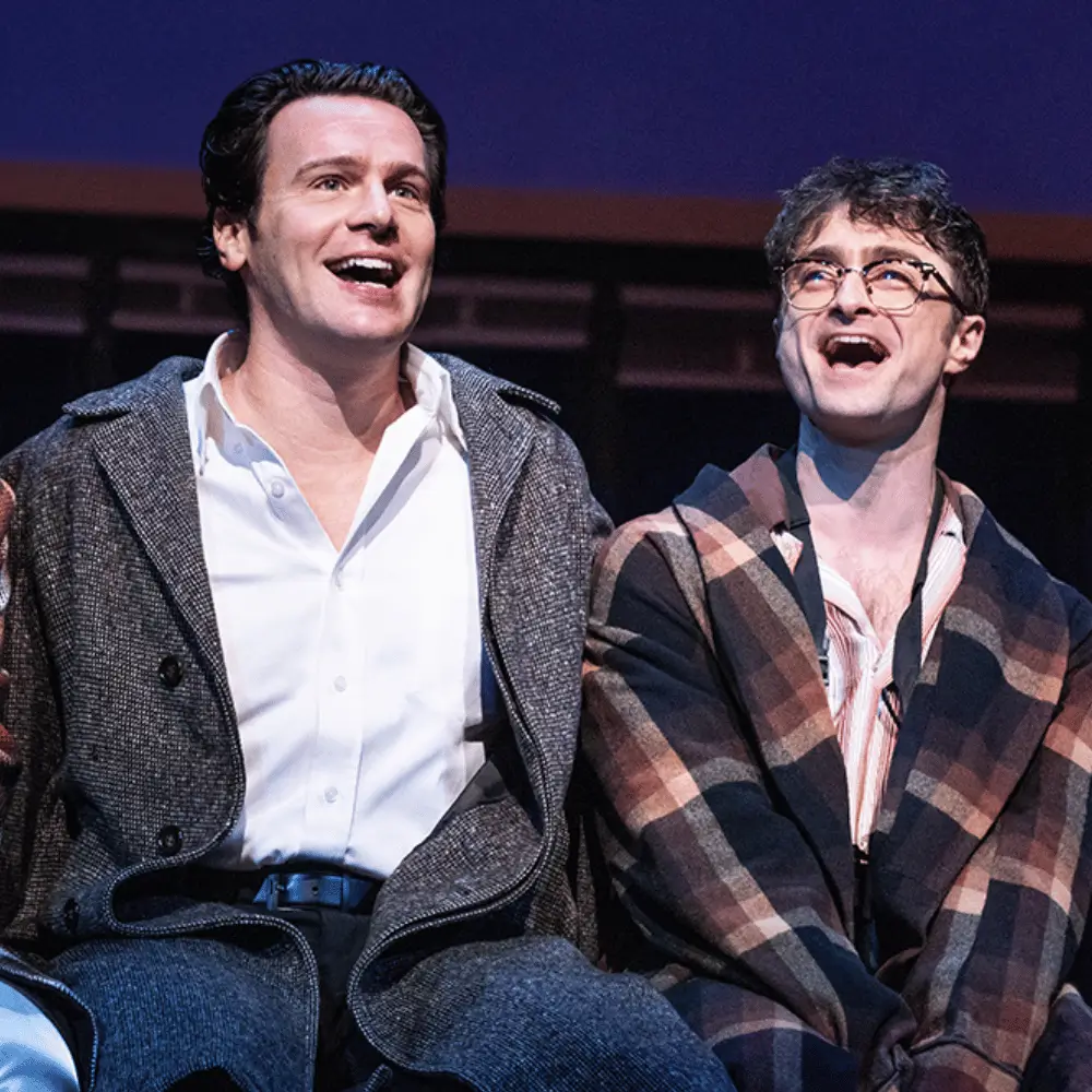Two star performers laughing together on stage during a Broadway musical