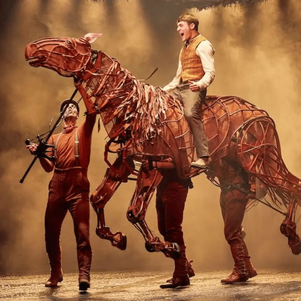 An actor riding a life-size horse puppet guided by a puppeteer in War Horse