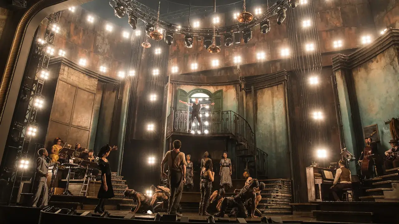 Performers bathed in warm lantern light on the industrial set of Hadestown